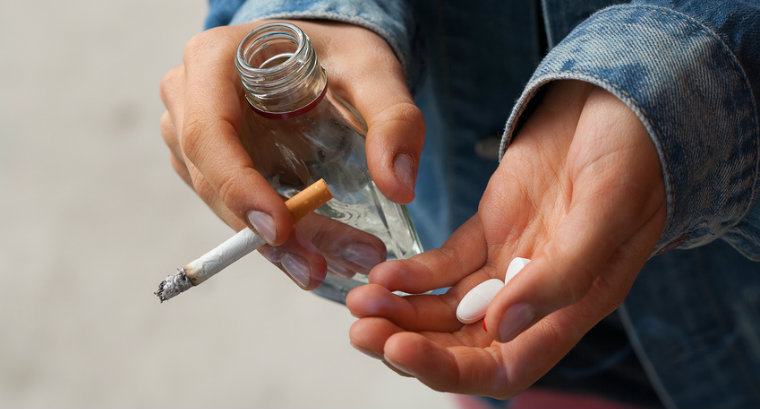 A person holding drugs, a cigarette and bottle