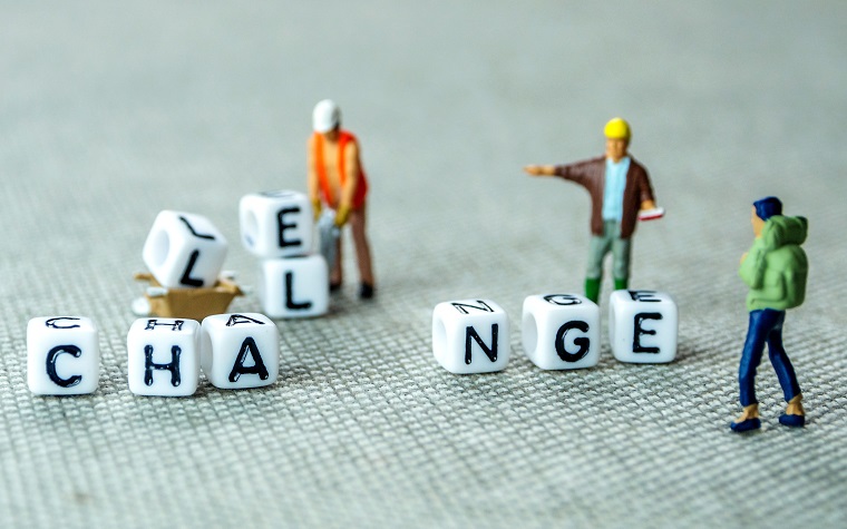 Letter cubes spelling out CHANGE with the LLE of 'challenge' being moved out of the way by toy people