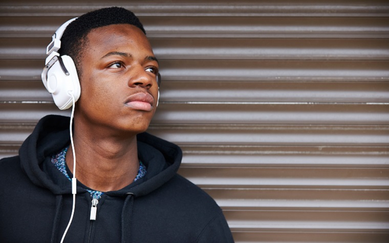 Black teenage boy leaning against a garage door listening to music