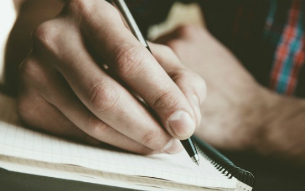 male hand writing in notebook with pen