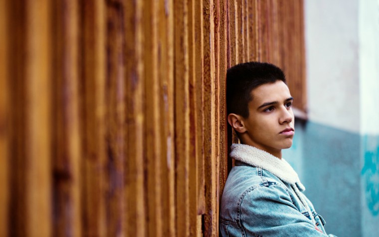 Young pensive guy on the background of an old wooden wall
