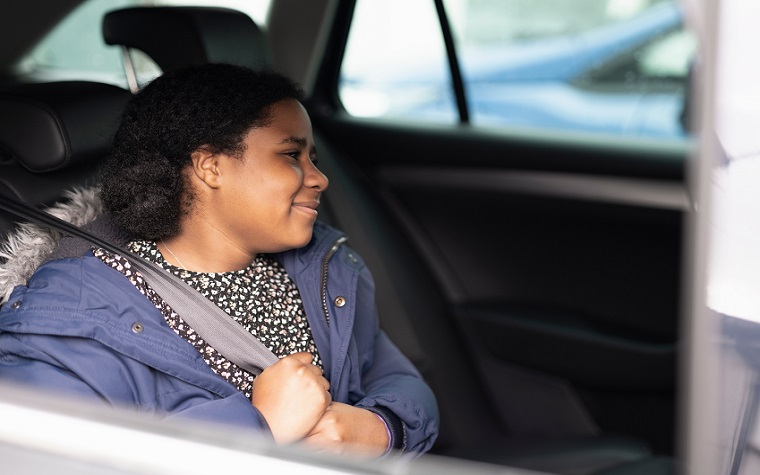 Girl around 12 putting seat belt on in the back of car