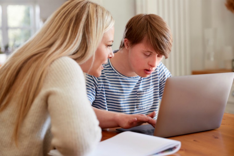 Young person with Down's syndrome on his laptop having help from friend/family member