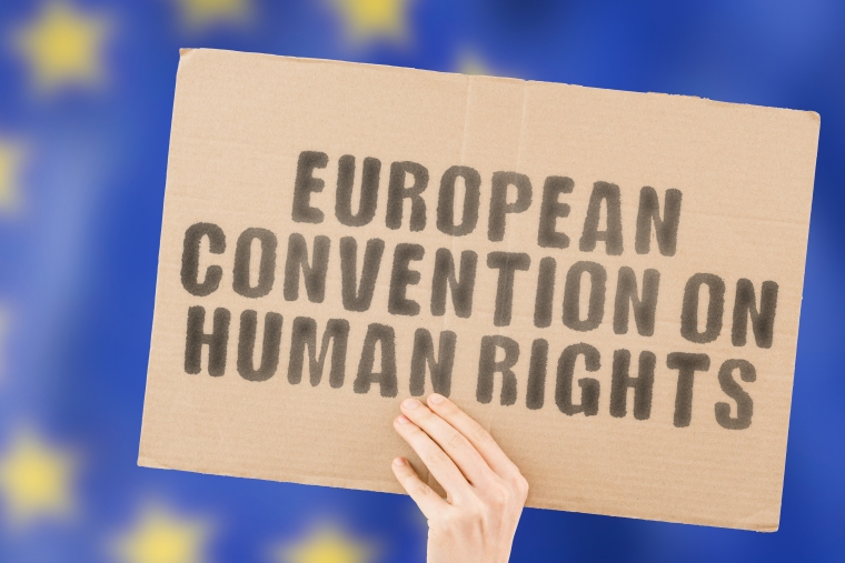 The phrase "European Convention on Human Rights " on a banner in men's hand with blurred European Union flag on the background.