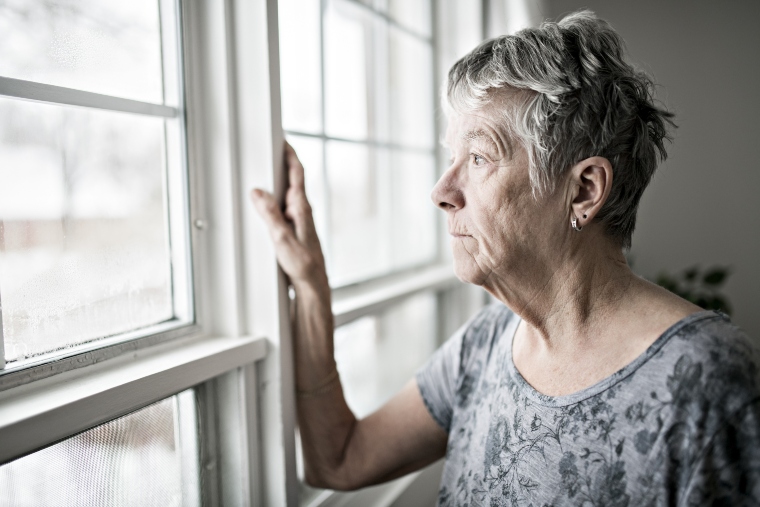 An older woman looking out of her window
