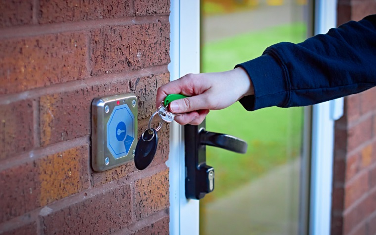 A person's hand waving fob over secure entry system
