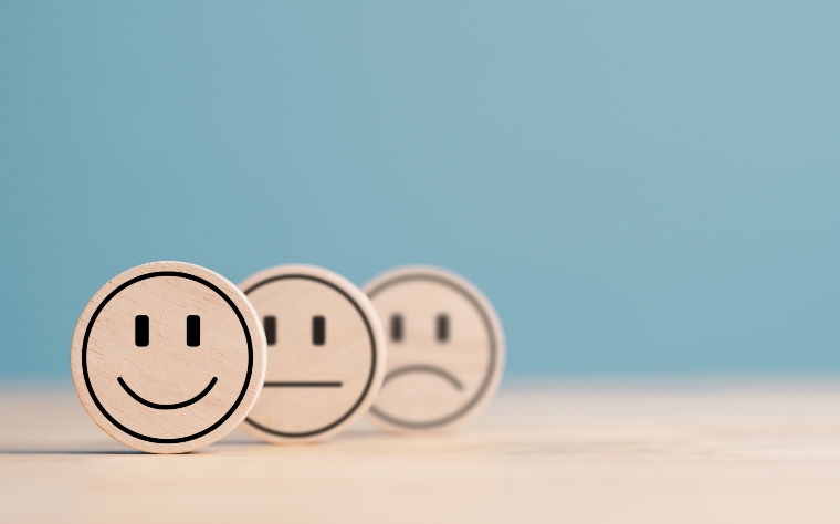 Three wooden circles with happy, normal and sad face icons, the happy icon is closest to the camera