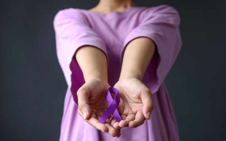Woman's torso wearing a purple top holding out her hands with a purple domestic abuse awareness month ribbon