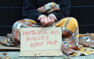 Homeless person on street with sign saying 'homeless and hungry please help'