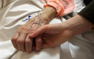 Close up on someone holding an older person's hand which has a canula in hospital