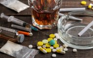 Various addictive drugs including alcohol, cigarettes, and drugs on a brown wooden table