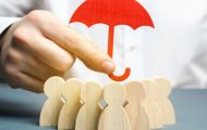 hand holding a cardboard red umbrella over wooden figures to signify safeguarding