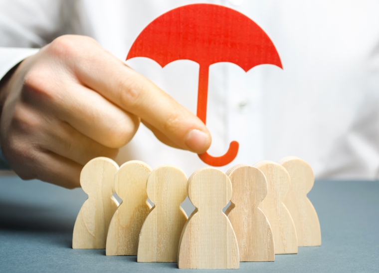 hand holding a cardboard red umbrella over wooden figures to signify safeguarding
