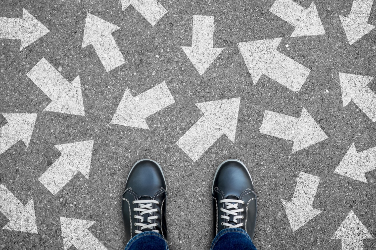 Looking down onto a pair of feet in shoes with arrows pointing in different directions on the floor to illustrate decisions