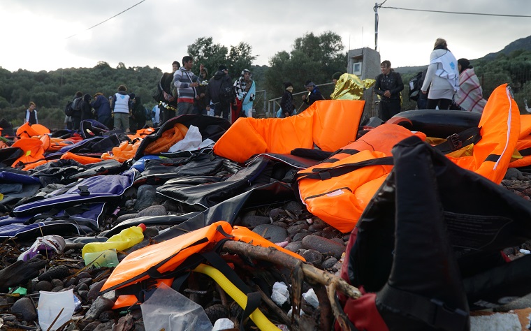 people of different ages gathered near abandoned belongings and life jackets on the shore - illegal immigration