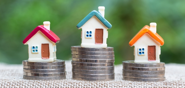 Miniature houses resting on coin stacks, concept for property and financial matters