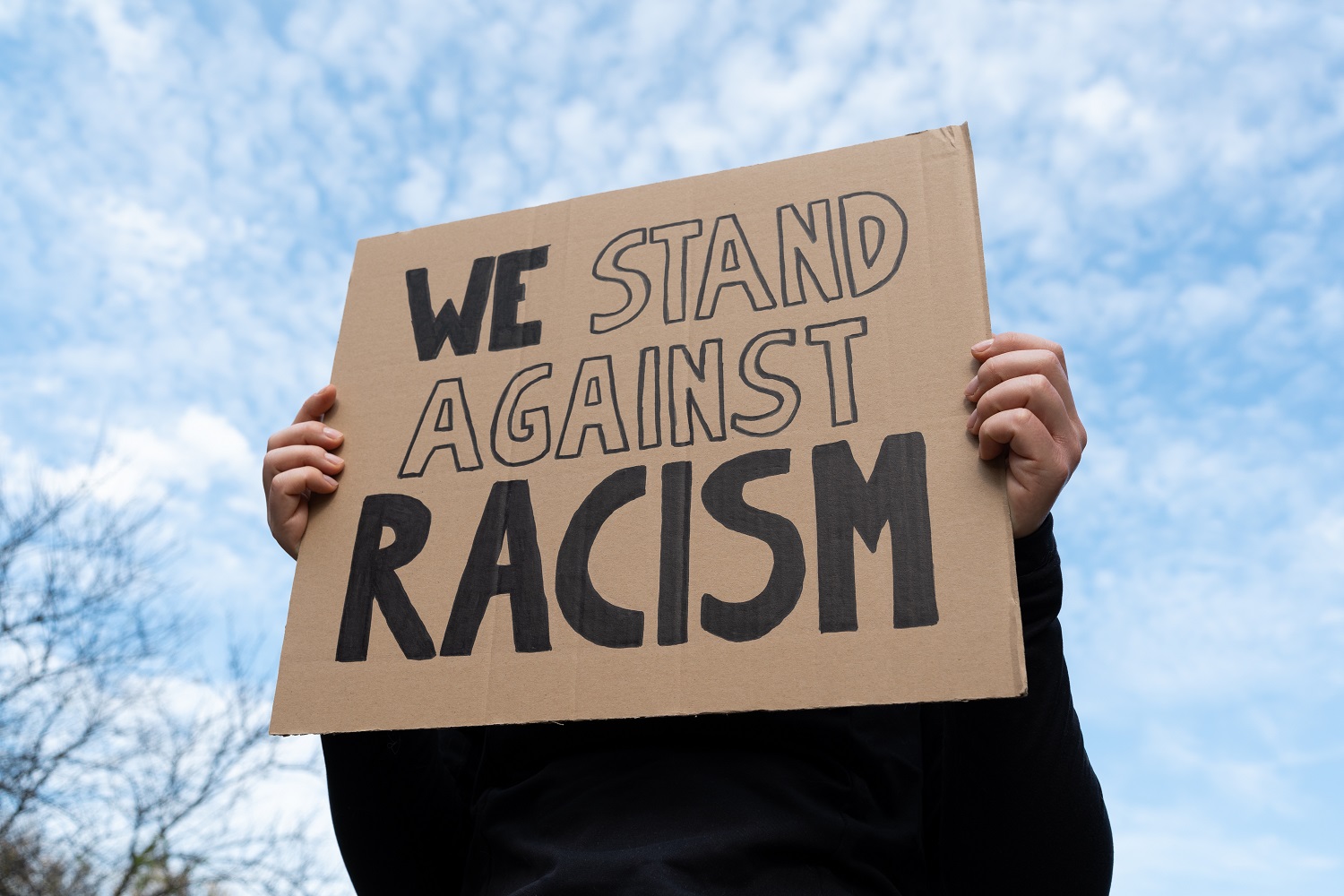 Person holding a placard reading 'we stand against racism'