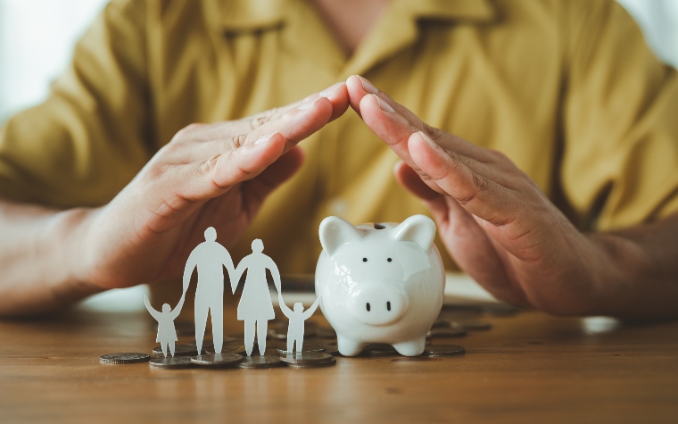 Hands protecting piggy bank and paper cut-out family finance money