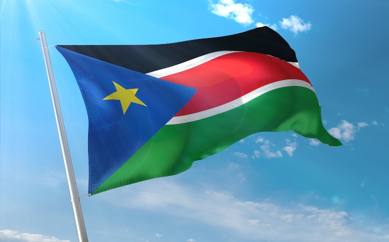 The South Sudan flag which has three broad horizontal stripes of black, red, and green (top to bottom), with two narrower white horizontal stripes separating the black and red and the red and green stripes, and a blue triangle at the hoist, within which is a five-pointed yellow star