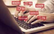 Close-up of someone's hands on a laptop with words like 'idiot', 'loser' appearing in speech bubbles to illustrate online trolls