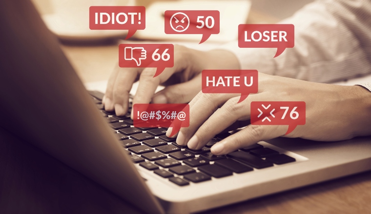 Close-up of someone's hands on a laptop with words like 'idiot', 'loser' appearing in speech bubbles to illustrate online trolls