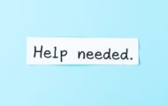 white paper note with the phrase 'help needed' written in black against a light blue background