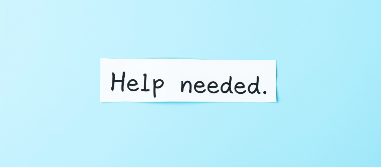 white paper note with the phrase 'help needed' written in black against a light blue background