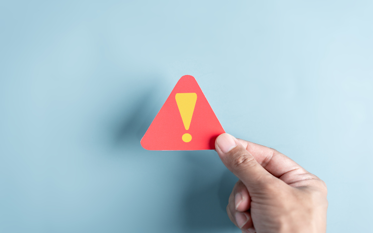 A hand holding a red triangle with a yellow exclamation mark inside to illustrate a warning or alert