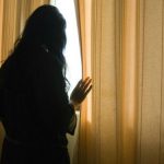 scared woman looking out of curtains