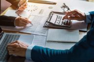 Image of men with laptop, calculator and finance reports (Credit: lovelyday12 / Adobe Stock)