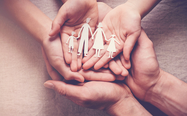 Image of joined hands holding a paper cutout of a family(Credit: sewcream / Adobe Stock)
