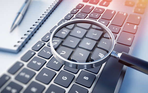 Image of magnifying glass, notebook and keyboard (credit: peterschreiber.media / Adobe Stock)