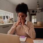 Image of young woman home working and looking tired and stressed (credit: StratfordProductions / Adobe Stock)