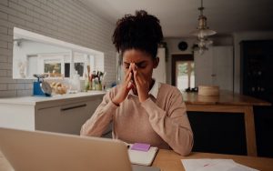 Image of young woman home working and looking tired and stressed (credit: StratfordProductions / Adobe Stock)
