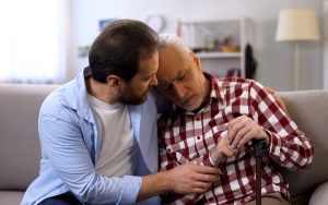 Middle-aged son comforting retiree terminally ill father, suffering pain, care