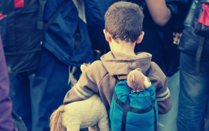 A young boy walking in a group with a small rucksack on his back, to symbolise asylum seeking