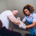 Care worker putting a bandage on a man's arm in his home.