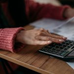Close-up of woman's hands with calculator and utility bills. The concept of rising prices for heating, gas, electricity. A lot of utility bills and hands in a warm sweater on a calculator