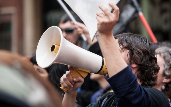 Unidentified young demostrator with megaphone and notebook protesting against austerity cuts