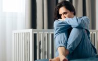 Woman looking depressed next to a cot, suggesting post-natal depression