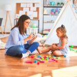 Young therapist woman speaking and treating child, counselor and behaviour correction at pedagogue payroom taking notes on clipboard