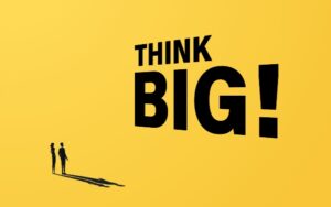 The words 'Think big' in capitals with an exclamation mark on a yellow background with the small figures of a man and woman looking up at the words