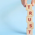 Person building tower of blocks spelling out 'trust'