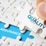 Person putting jigsaw piece with word 'quality' written on it on to space with 'assurance' written on it