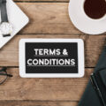 Terms and Conditions text, Office desk with electronic devices, computer and paper, wood table from above, concept image for blog title or header image.