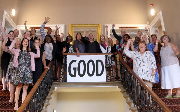 medway staff on a staircase, some with their arms in the air. Everyone is smiling and there is a banner saying 'good' hanging off the top of the staircase