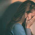 A blonde female covering her face with her hands.