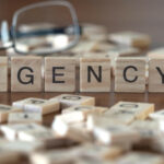agency word or concept represented by wooden letter tiles on a wooden table with glasses and a book