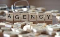 agency word or concept represented by wooden letter tiles on a wooden table with glasses and a book
