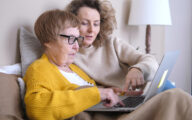 Woman helping older relative fill out online assessment form on computer